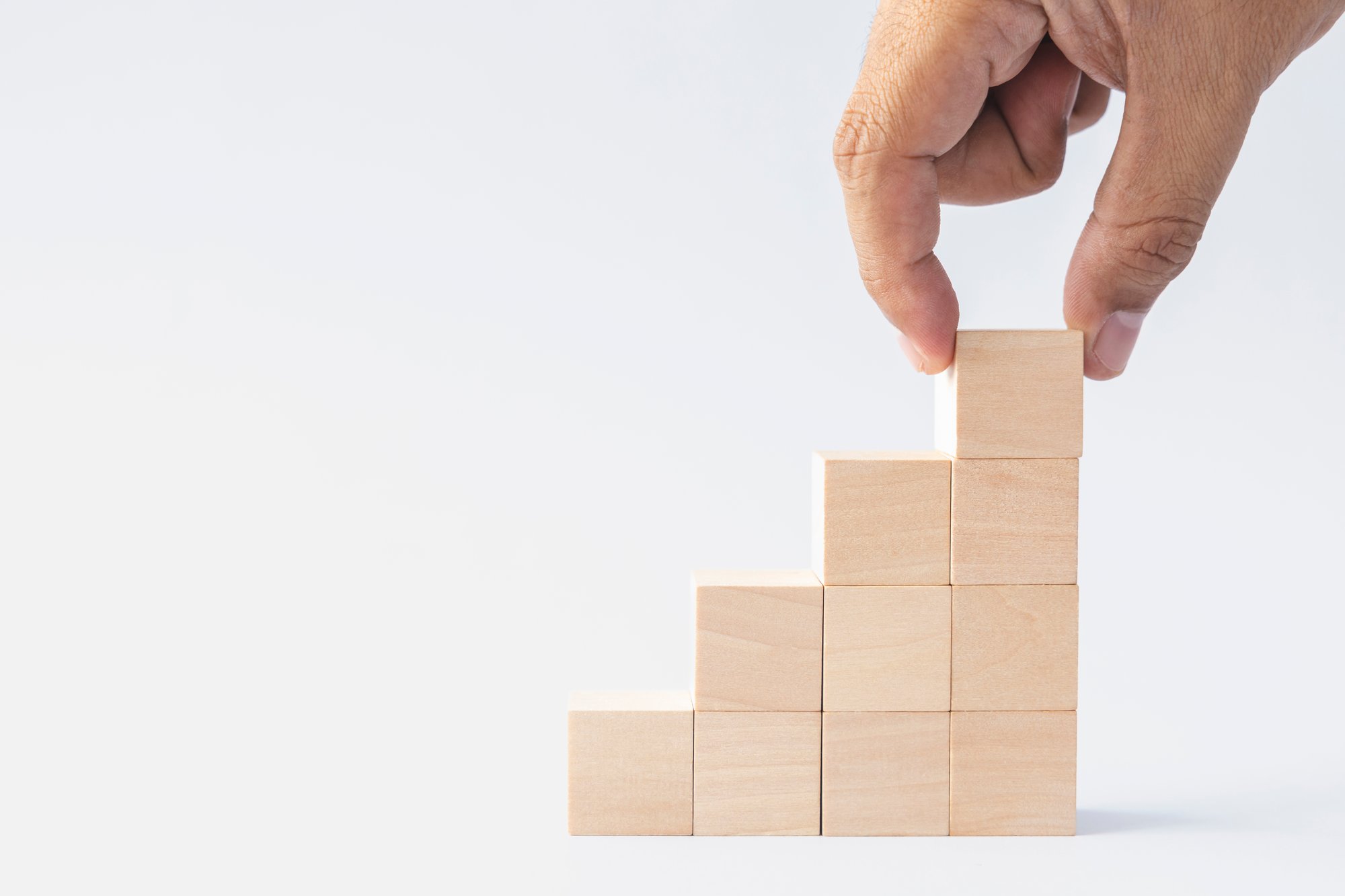 A man's hand building a structure with square wooden blocks.