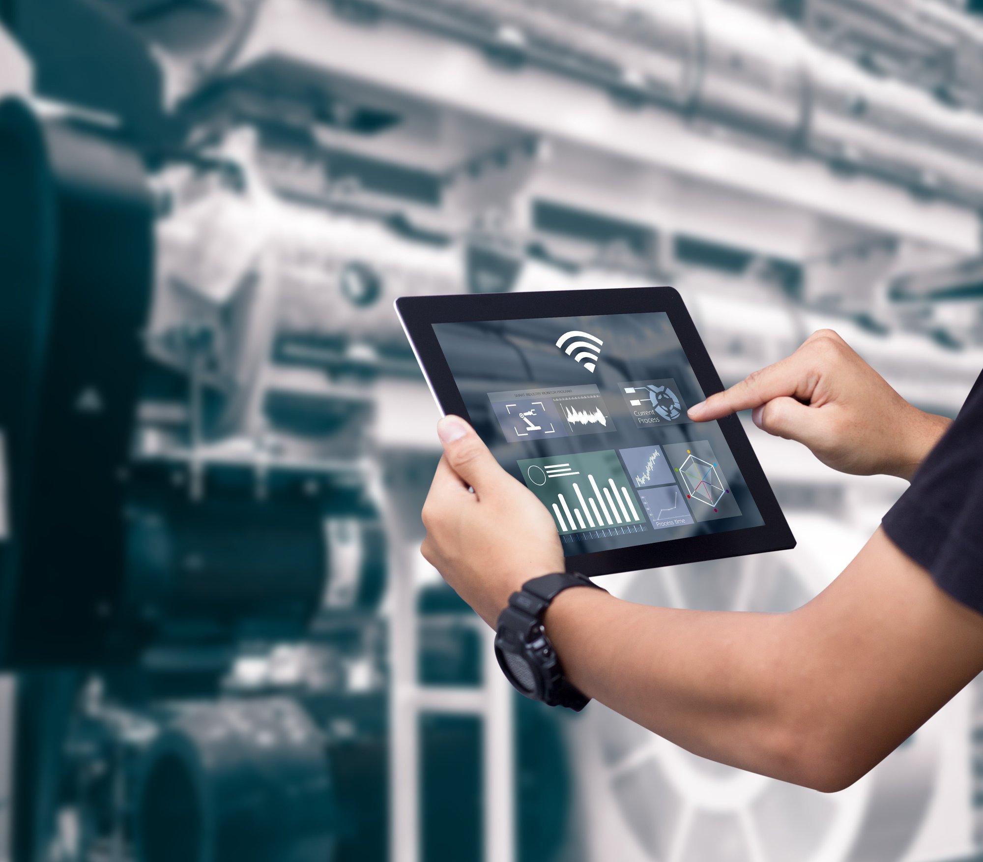 A man is seen from behind holding a tablet. The screen displays a dashboard with monitoring KPIs.